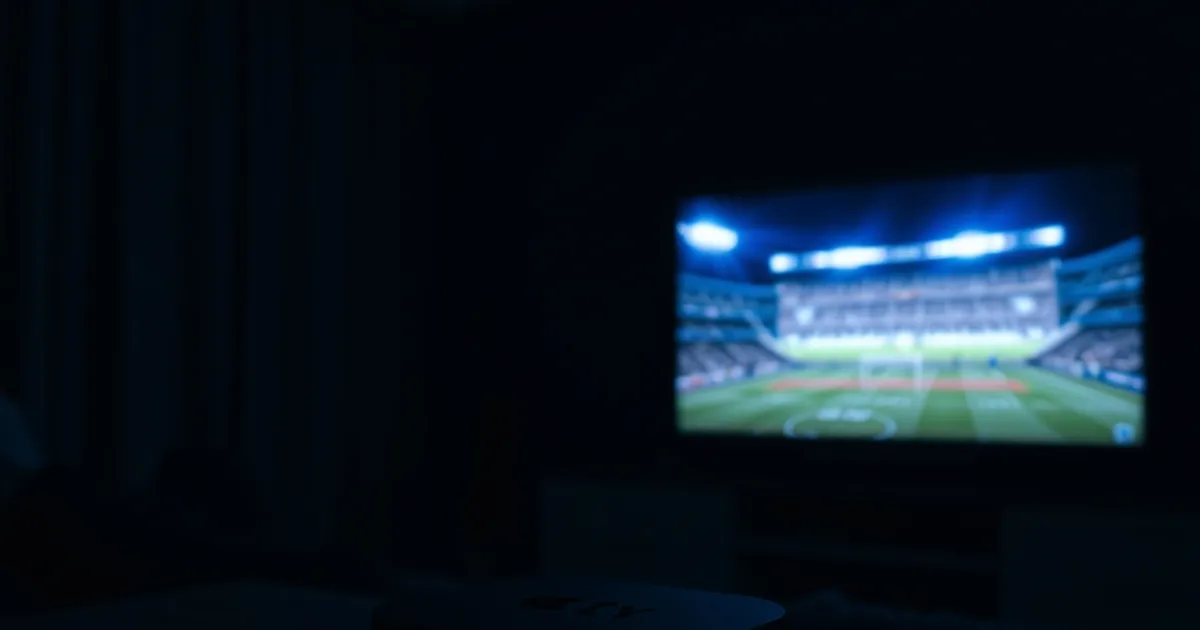 Apple TV set-top box glowing on a dark media console with a football match lighting up the TV screen behind it
